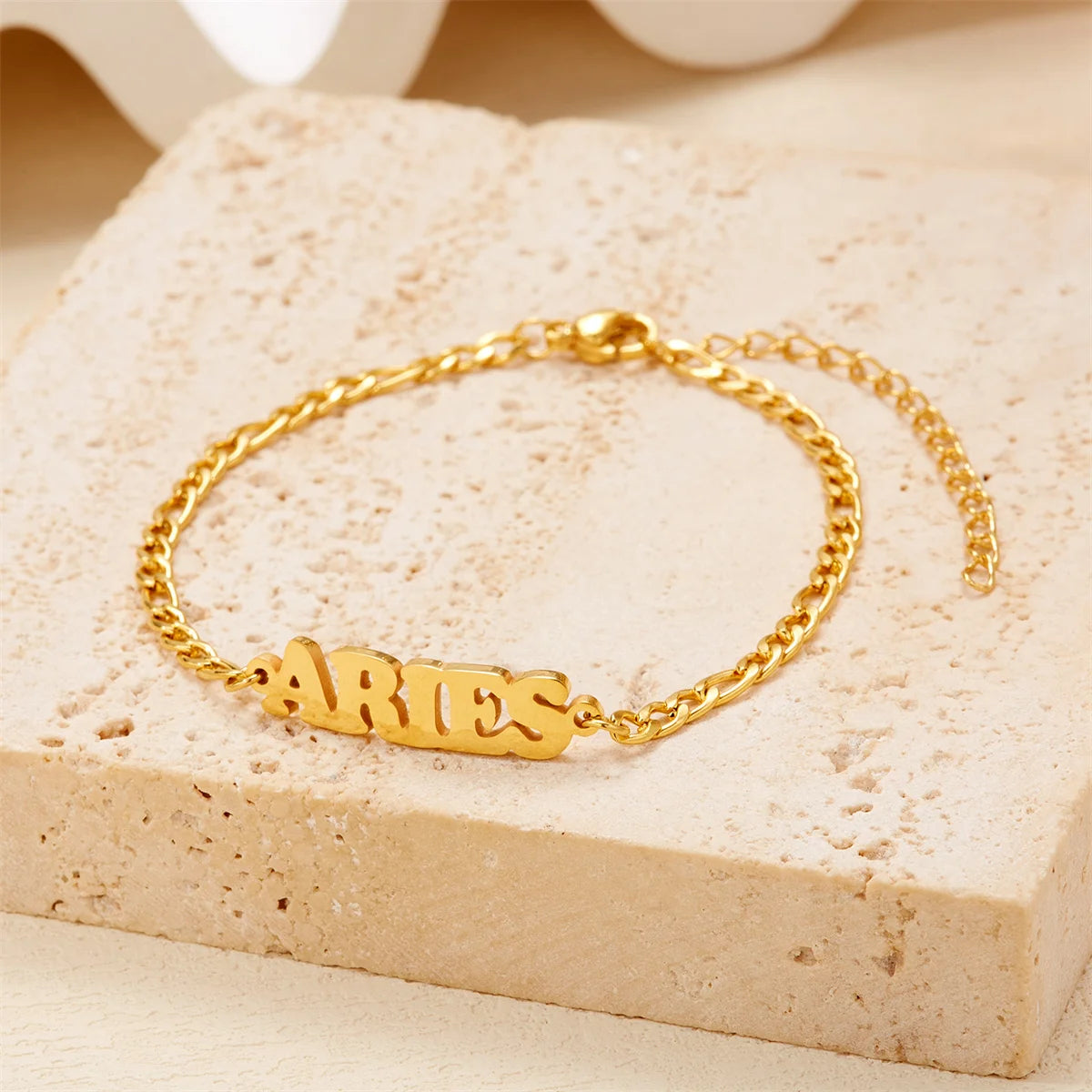 Gold stainless steel zodiac constellation charm bracelet resting on a light beige surface.