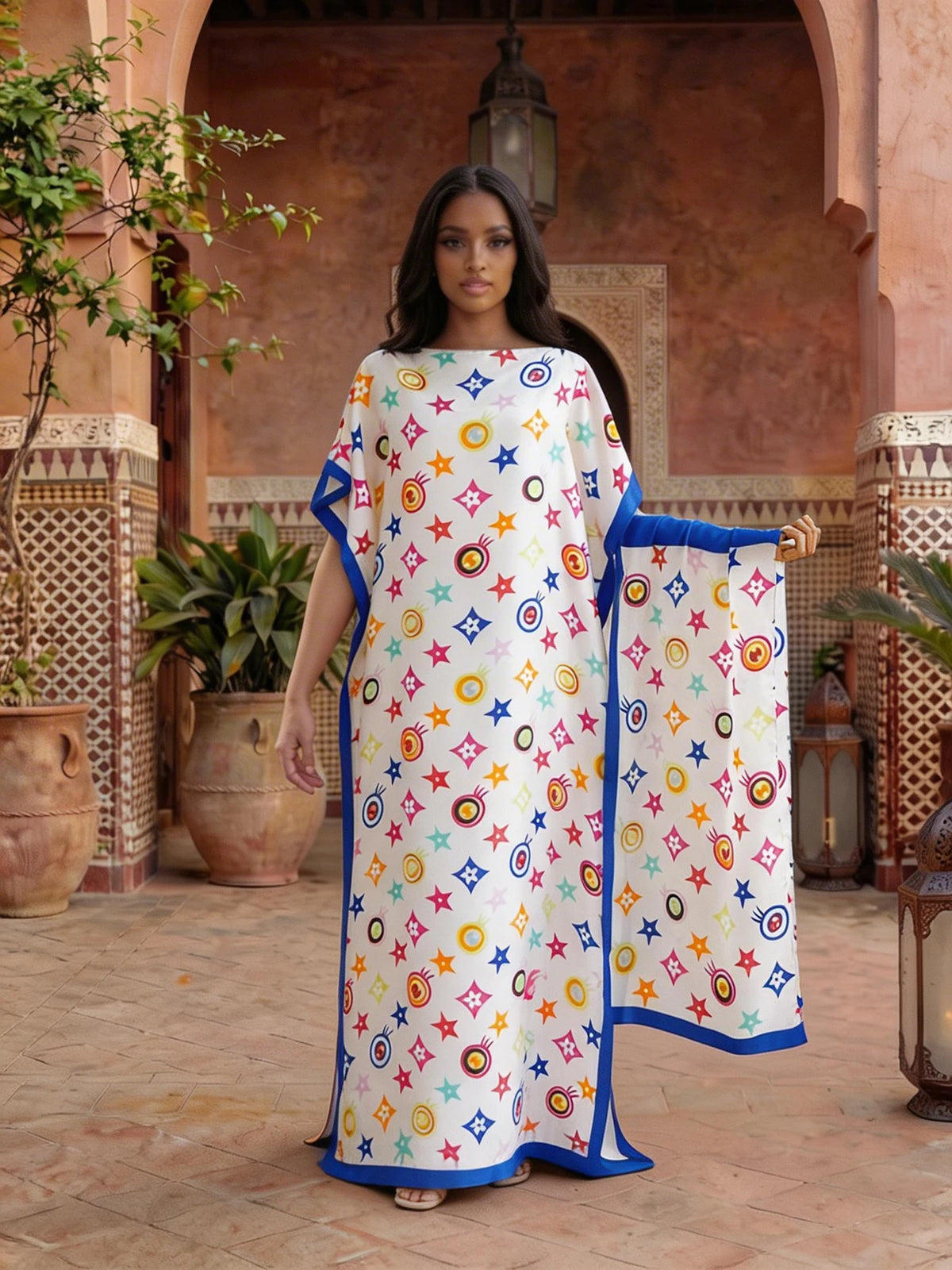 A woman models a floral print satin maxi shawl in white and blue on an outdoor patio.