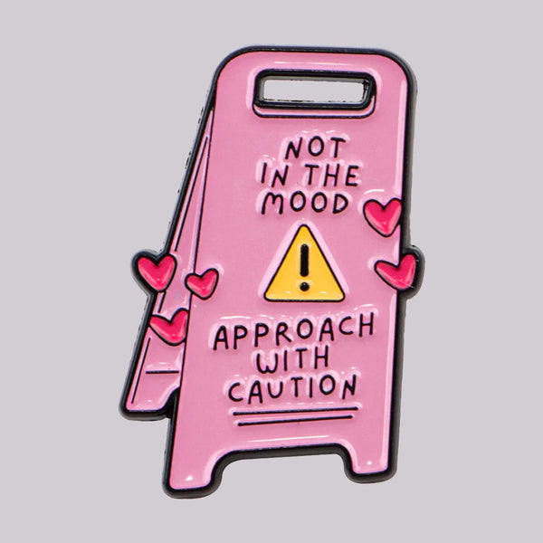 A pink enamel pin featuring a warning sign that reads Not in the mood, approach with caution.