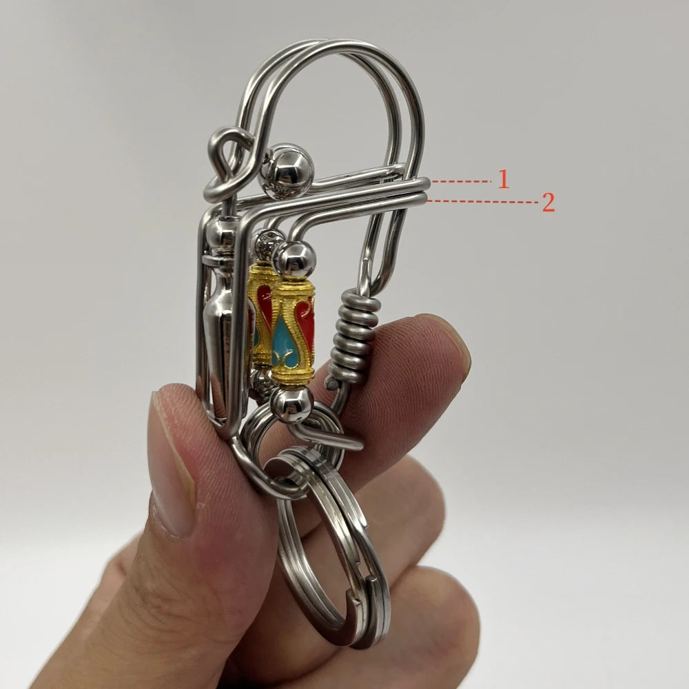 Un porte-clés mécanique en acier inoxydable avec un fermoir et des éléments décoratifs tenu dans une main.