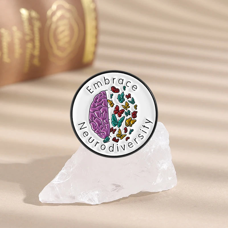 An enamel lapel pin featuring a purple brain shape surrounded by colorful flowers and the text Embrace Neurodiversity
