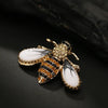 Broche dorée en forme d'abeille avec des marques noires et blanches sur fond sombre.