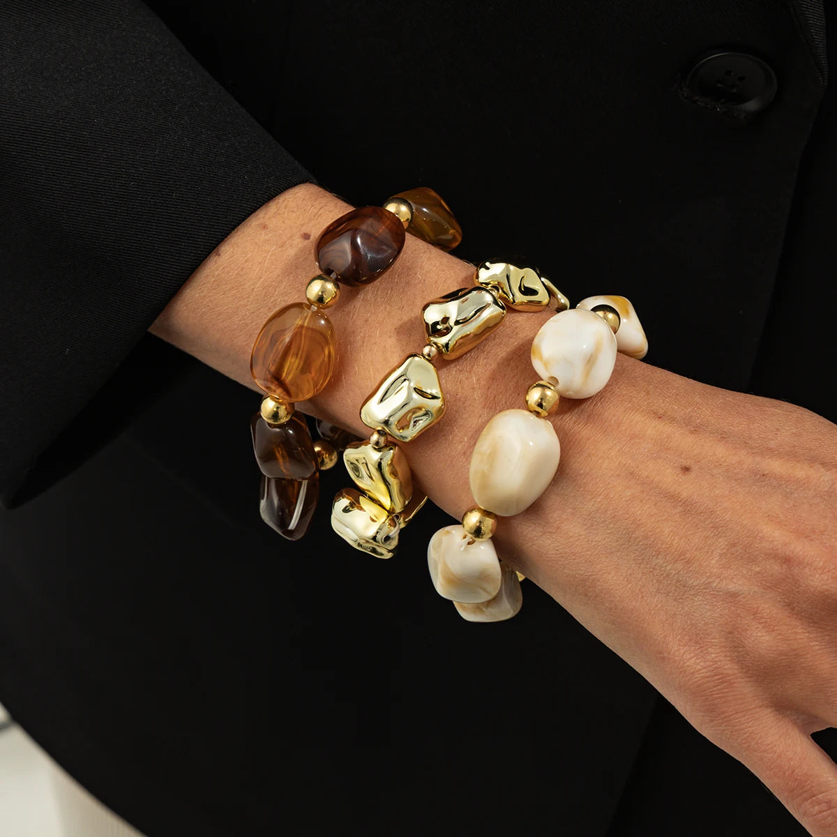 Une main portant un ensemble de bracelets vintage en résine acrylique bohème avec des perles d'ambre et d'or.