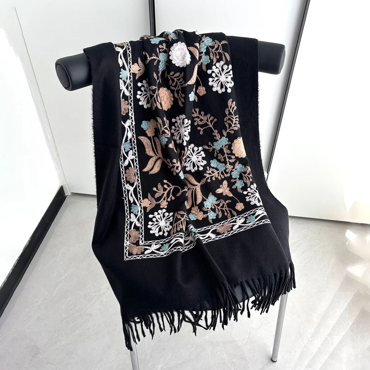 A black luxury floral scarf featuring gold and blue embroidery with white accents displayed on a hanger.