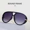 Gafas redondas con marco negro y detalles dorados sobre una superficie blanca.