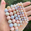 A hand holds a string of smooth round jade beads in various pastel shades of pink, white, and blue.