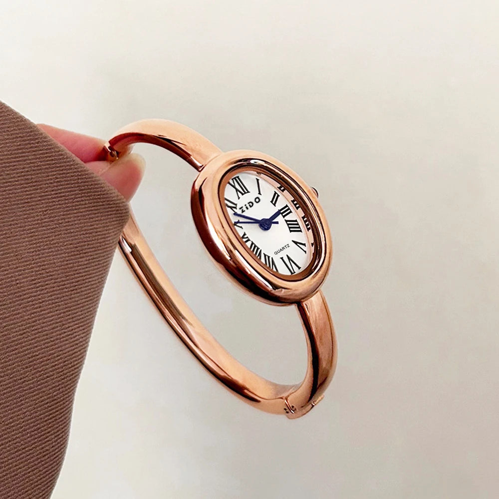 A close-up shot of a rose gold vintage quartz analog watch with an oval face being held by a hand.