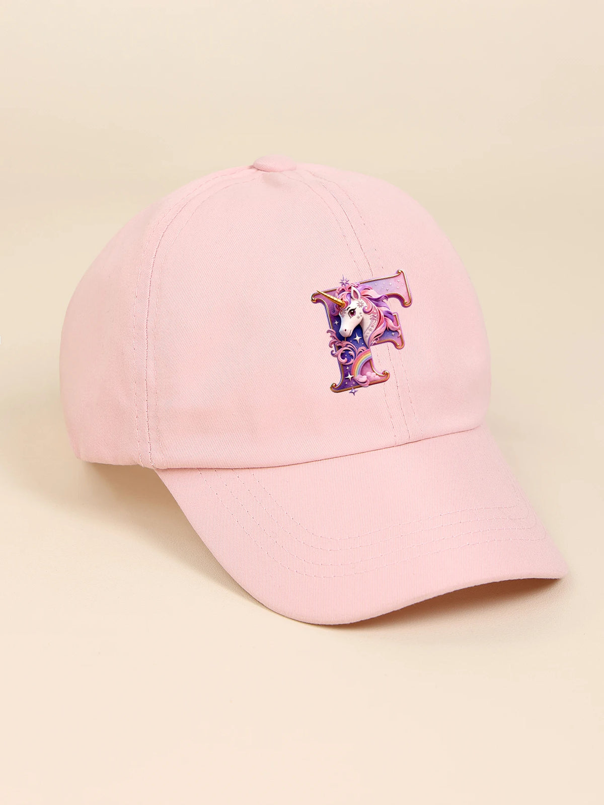 A pink baseball cap featuring a purple and iridescent unicorn letter design.