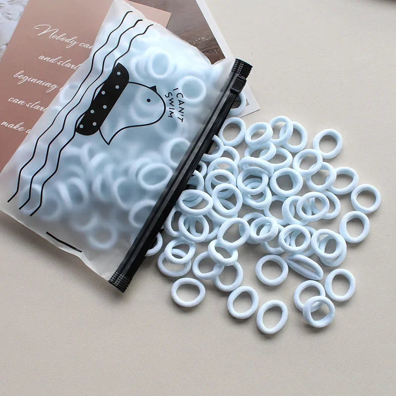 A pile of white elastic hair bands is shown next to a package featuring a cute animal design.