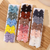 A collection of handmade ribbon bow hair clips in various shades of blue, green, brown, and purple displayed on a wooden surf