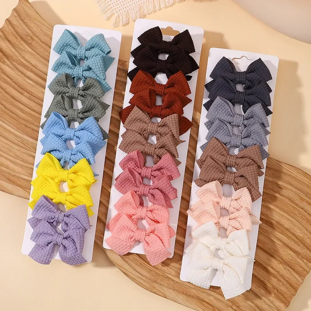 A collection of handmade ribbon bow hair clips in various shades of blue, green, brown, and purple displayed on a wooden surf