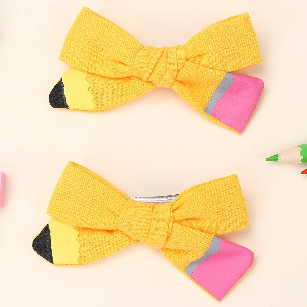 A set of yellow pencil-shaped bow hair clips with pink accents.