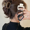 A hand is shown holding a set of square lightweight hair claw clips against dark brown hair.