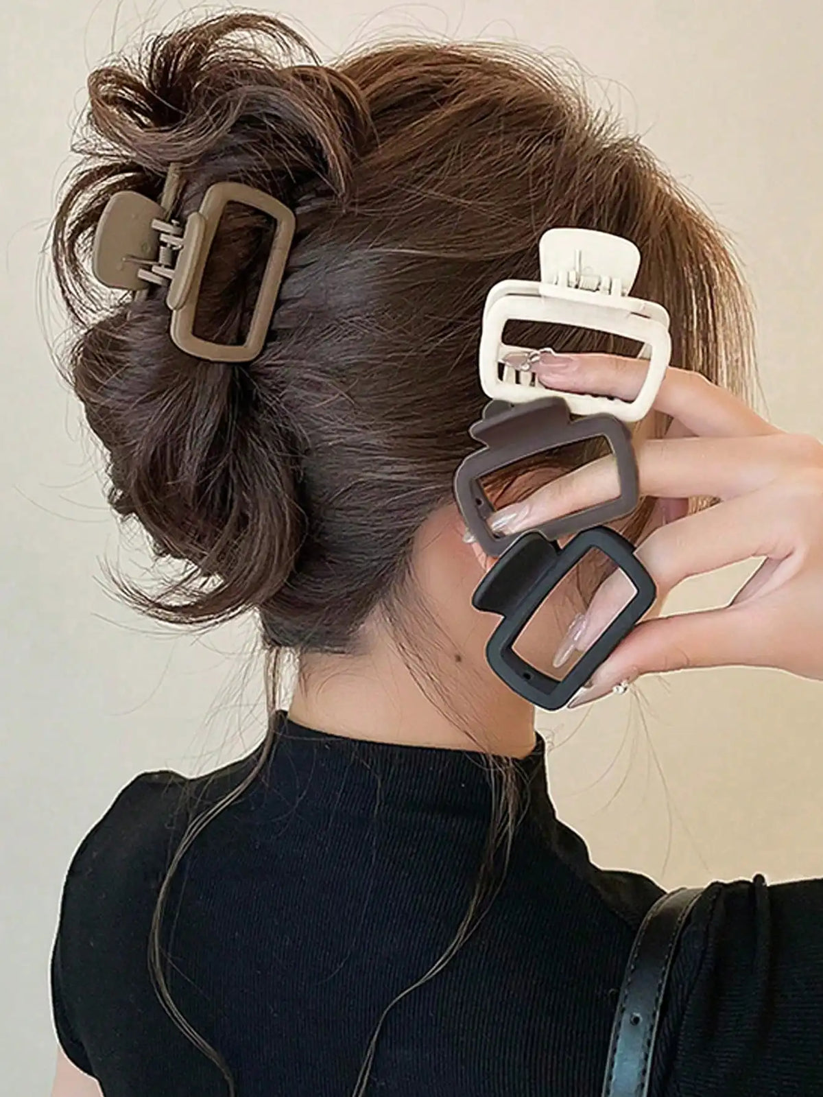 A hand is shown holding a set of square lightweight hair claw clips against dark brown hair.