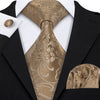 A close-up of a men's silk jacquard tie in gold and beige tones worn with a black suit jacket.