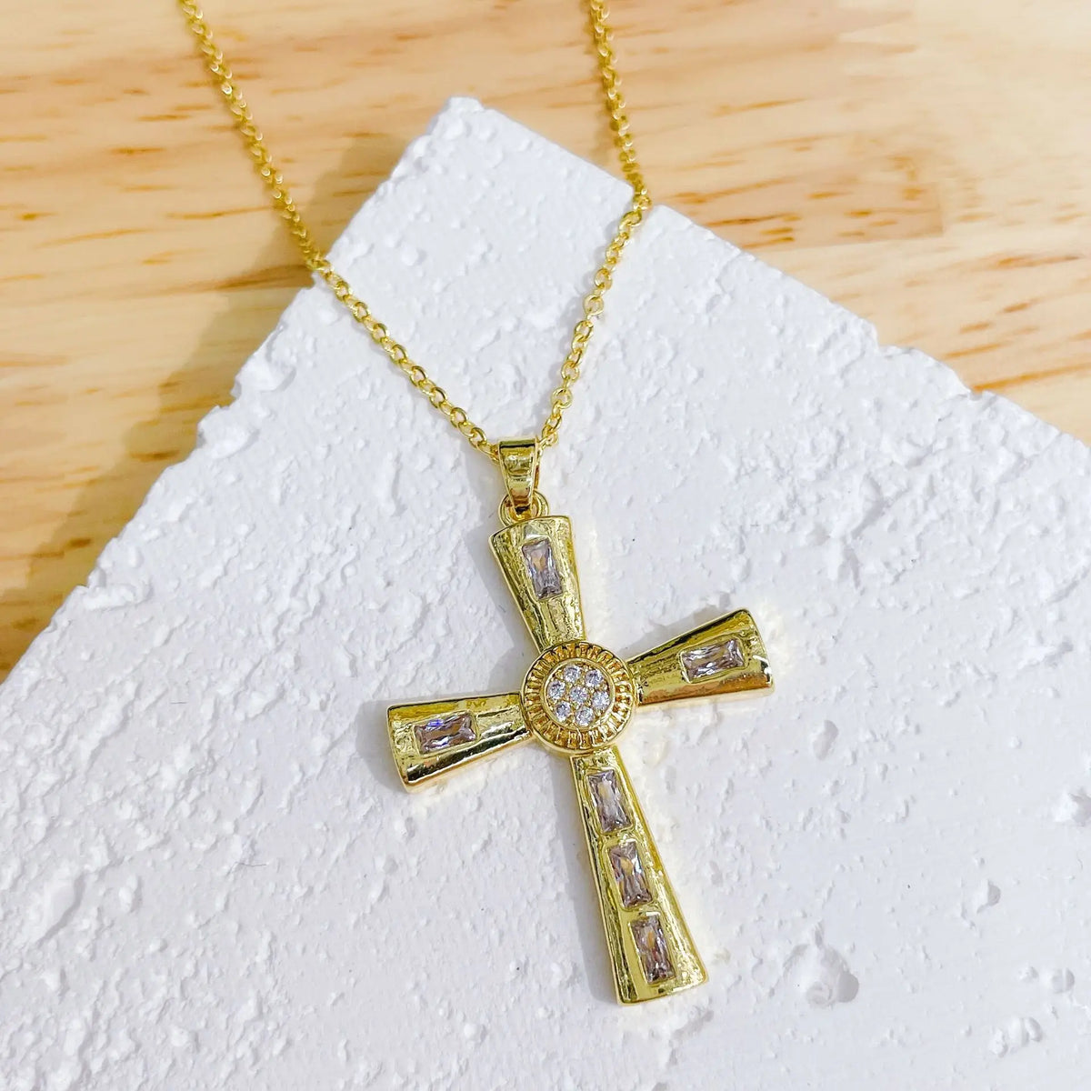 A dainty gold cross charm necklace with clear stones displayed on a white surface.