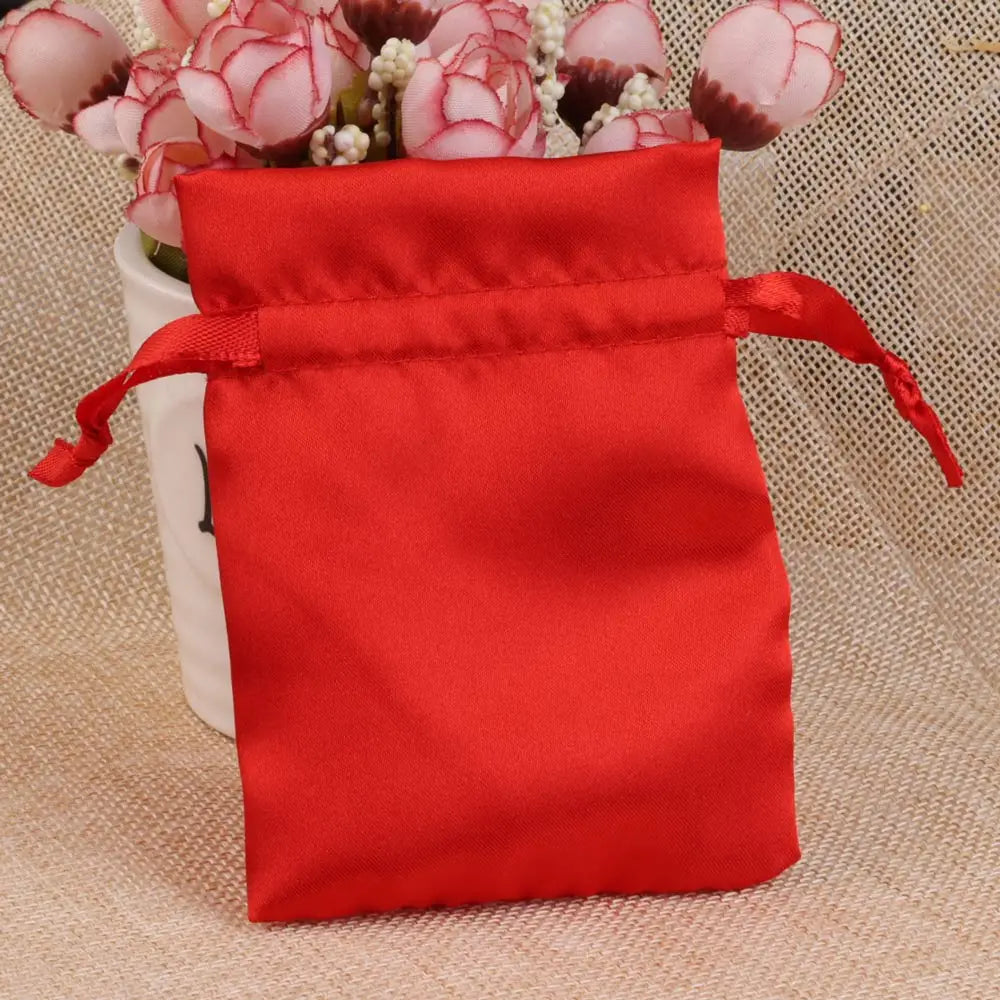 A bright red satin drawstring pouch filled with pink and white flowers.