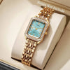 A gold-toned rhinestone quartz wristwatch with a light blue face and square bezel is displayed in a box.