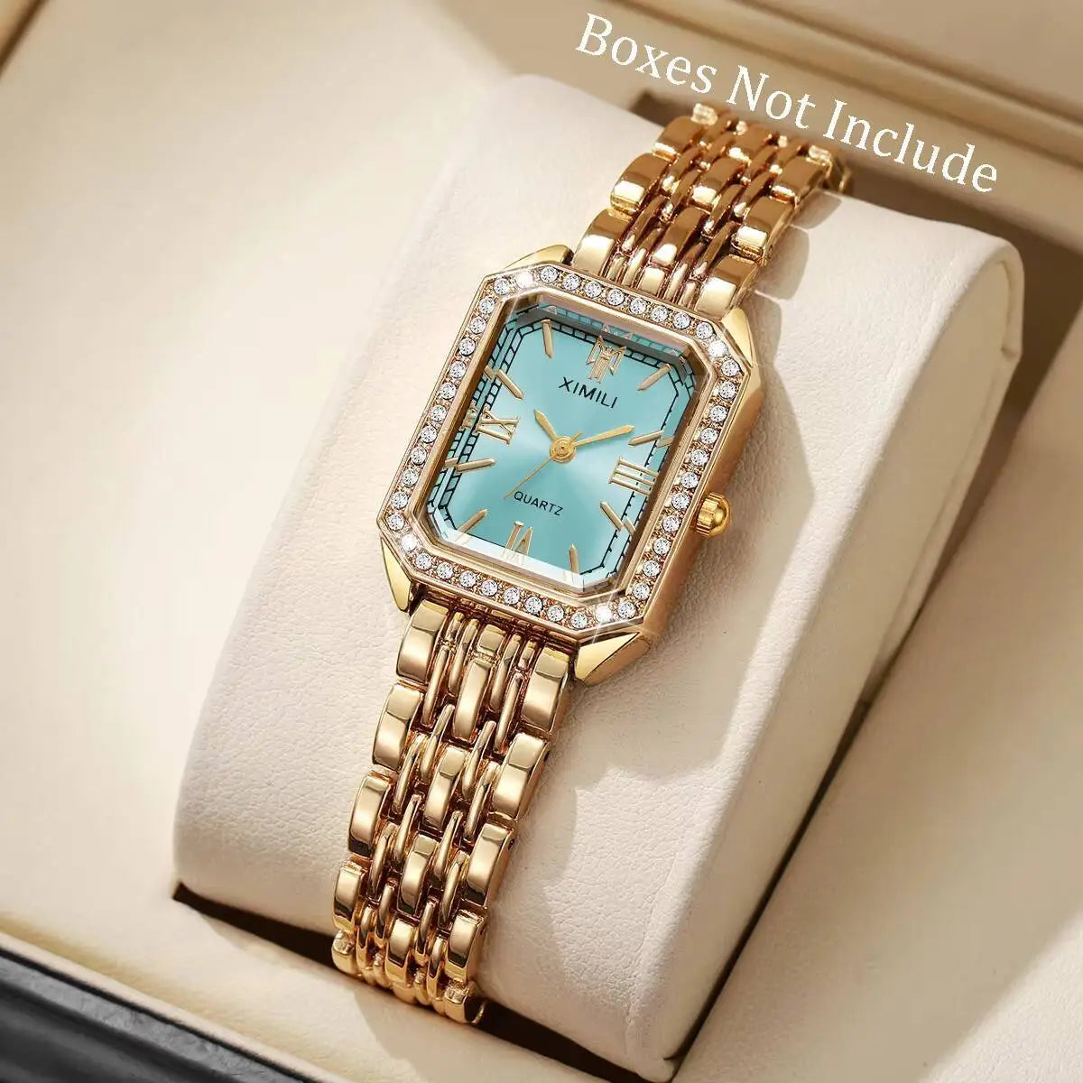 A gold-toned rhinestone quartz wristwatch with a light blue face and square bezel is displayed in a box.