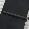 A close-up of a black business tie clip with a copper bar clasp resting on a dark surface.