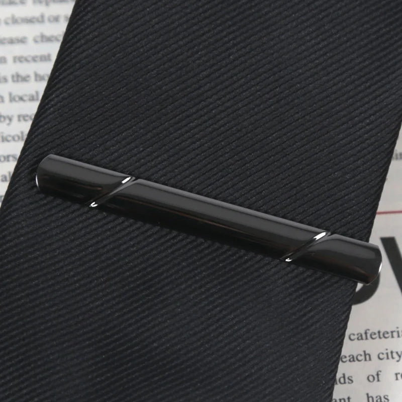 A close-up of a black business tie clip with a copper bar clasp resting on a dark surface.