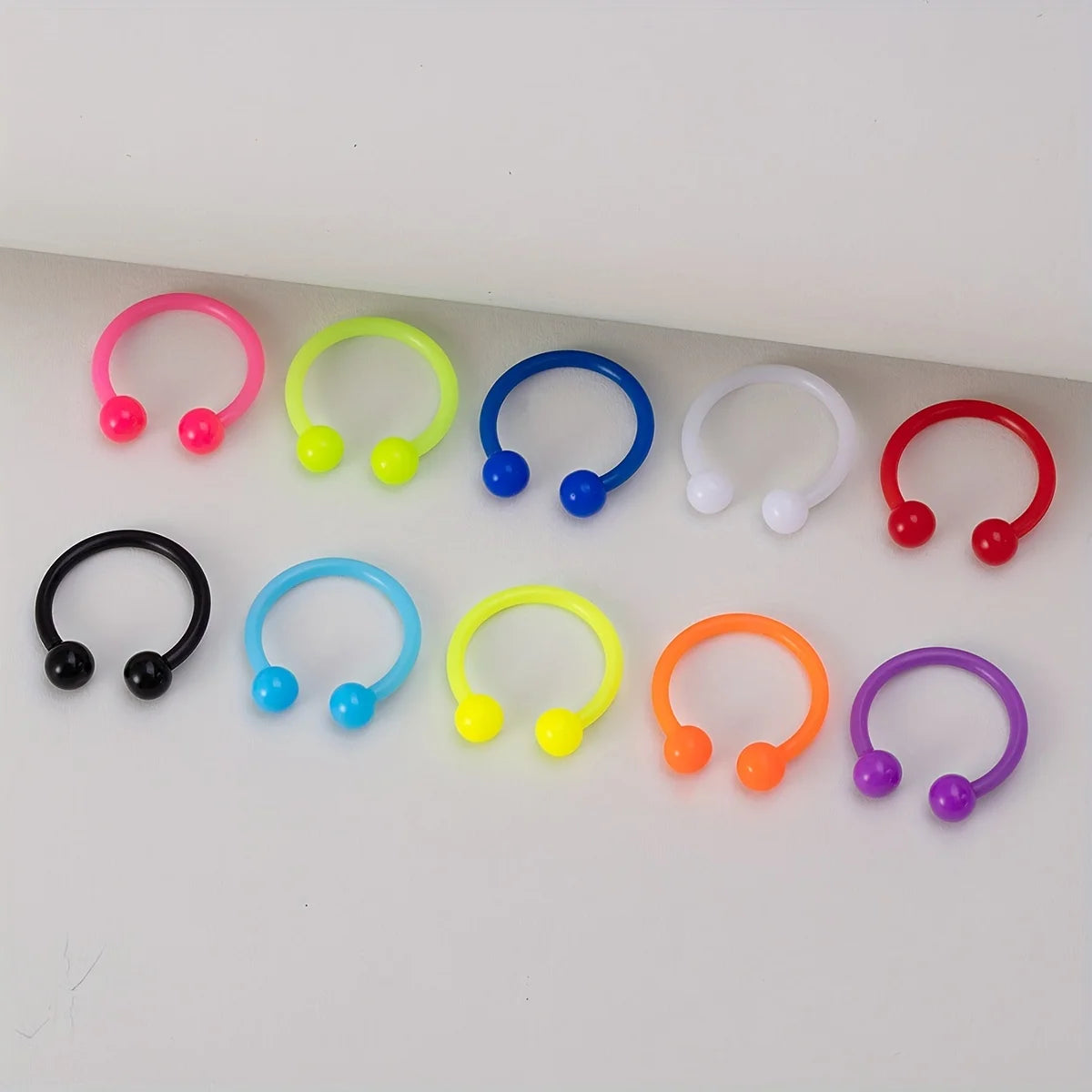 A collection of colorful flexible acrylic piercing jewelry rings in various colors like pink, yellow, blue, and red.