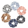 Un set de seis gomas para el pelo con estampado floral de satén en varios colores pastel y oscuros, dispuestos en círculo.
