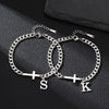 A silver stainless steel Cuban chain bracelet with a cross pendant is displayed on a dark surface.