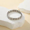 A silver stainless steel charm bracelet is displayed on a white stone surface.