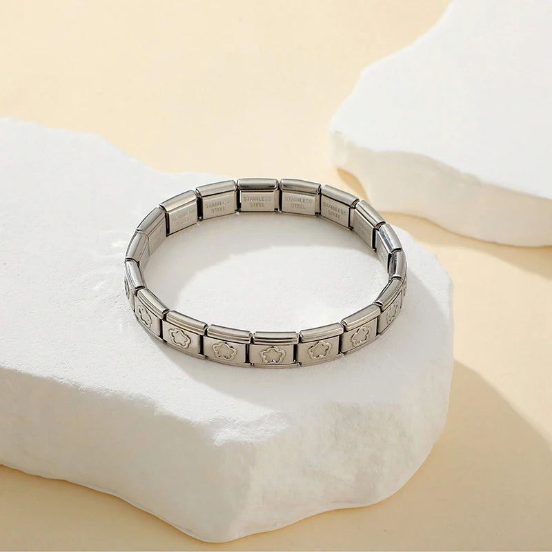 A silver stainless steel charm bracelet is displayed on a white stone surface.