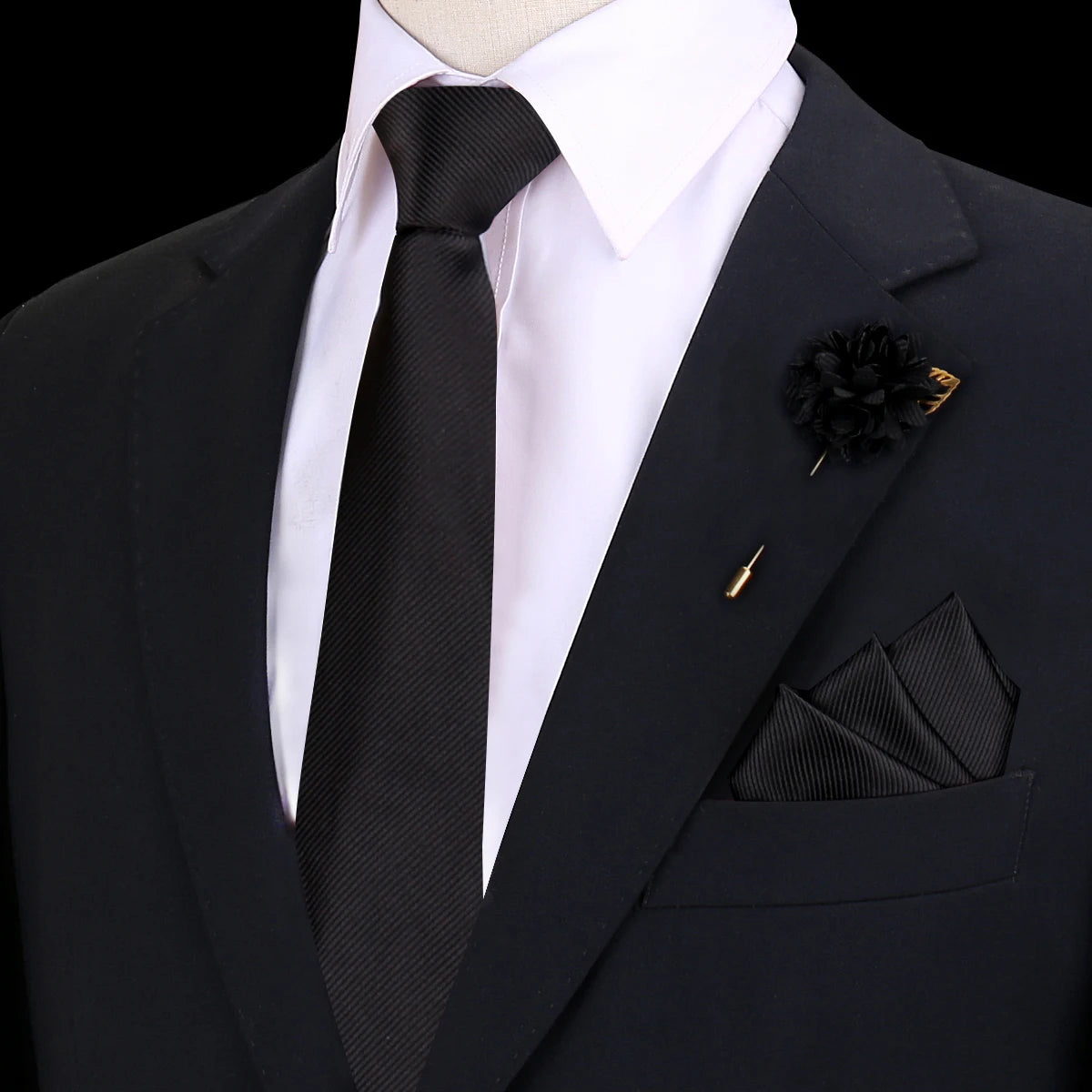 Chaqueta negra con camisa blanca, corbata de seda negra, pañuelo de bolsillo doblado y prendedor floral en la solapa negra.