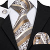 A close-up of a men's silk jacquard tie featuring silver and gold patterned fabric worn with a black suit jacket.