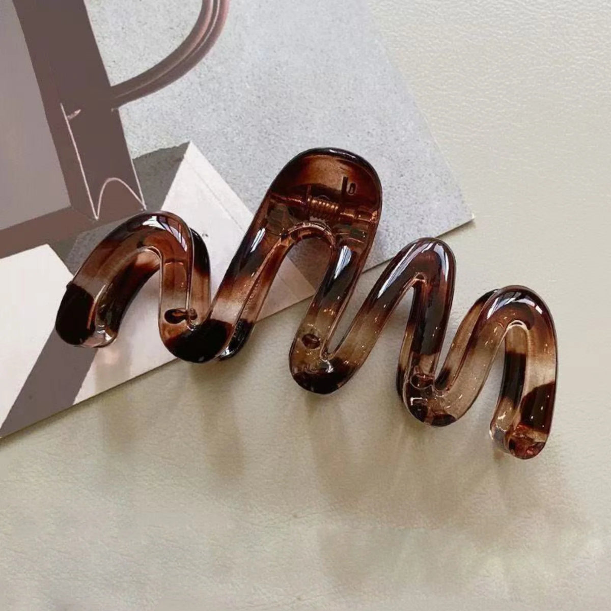 A pair of high-gloss amber hair clips shaped like a wavy line, displayed on a light surface.