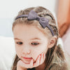 A young girl with light brown hair is shown wearing a gray grosgrain ribbon hair bow.