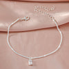 A delicate silver chain anklet with a sparkling zircon heart cross charm displayed on a pink fabric.