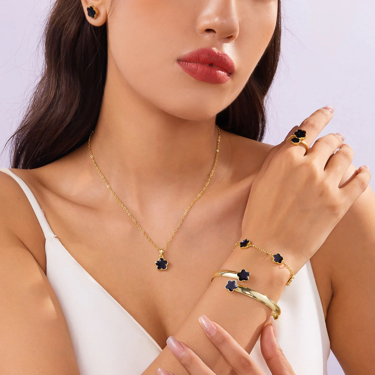 A close-up of a woman wearing a gold necklace and bracelet set featuring dark blue enamel plum blossoms.