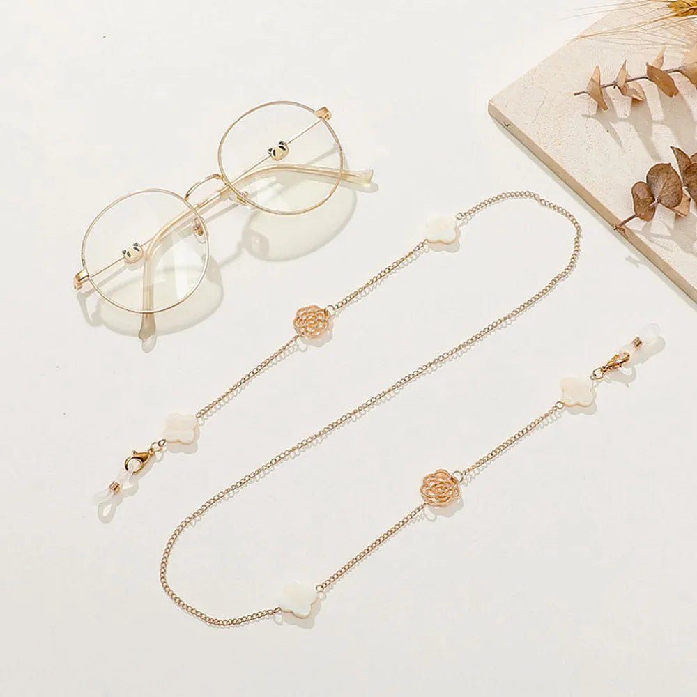 A delicate gold-toned chain necklace featuring small pearl and floral charms, displayed next to a pair of round wire-frame ey