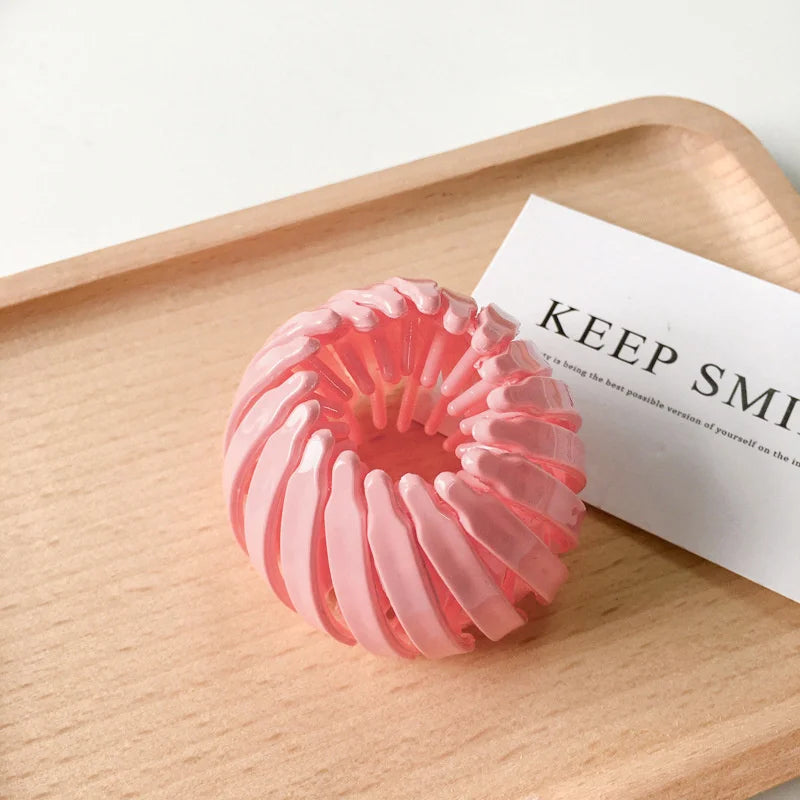 A pink, spiral-shaped hair clip is displayed on a wooden tray next to a card.