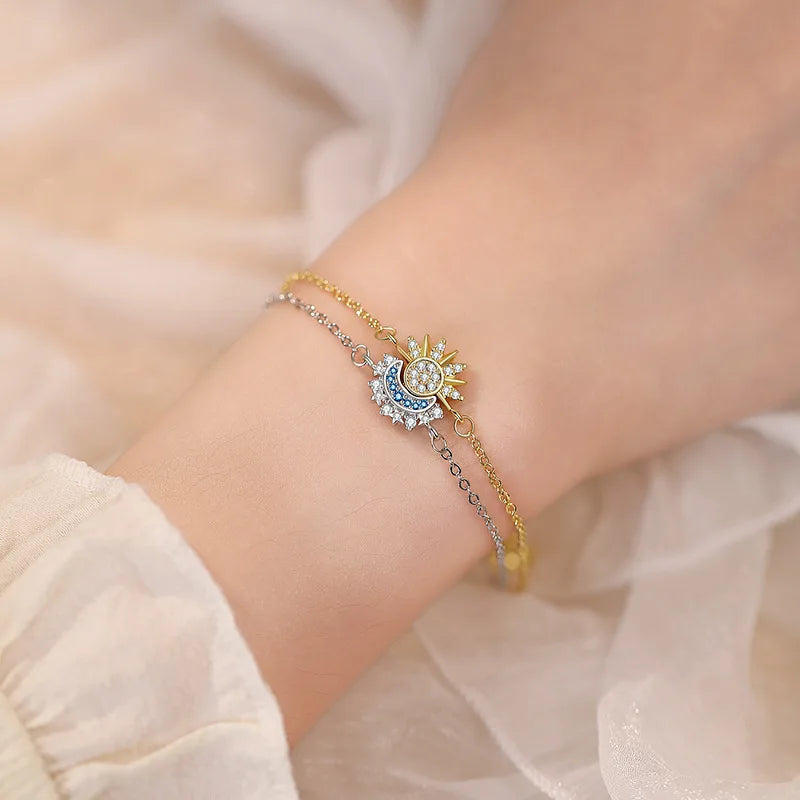 Nahaufnahme eines gold-silbernen, verstellbaren Armbandes mit Sonne- und Mond-Anhängern am Handgelenk.