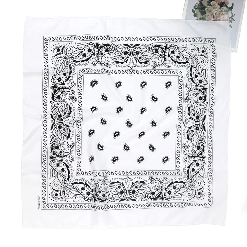 A white rectangular scarf featuring an intricate black paisley and floral pattern border.