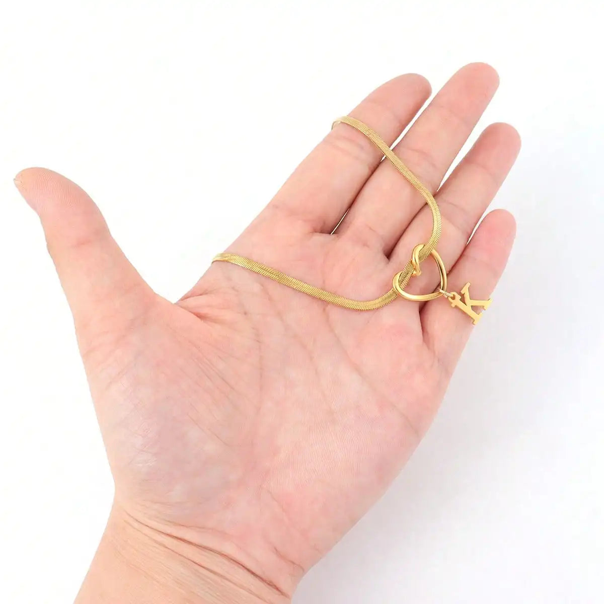 Eine Hand hält eine zarte goldvergoldete Initialherz-Kette mit einem kleinen Anhänger.