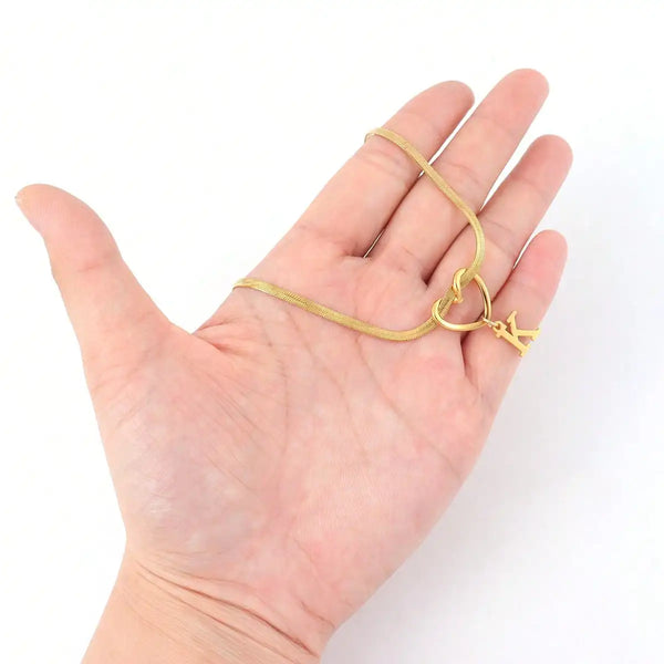 Eine Hand hält eine zarte goldvergoldete Initialherz-Kette mit einem kleinen Anhänger.