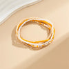 A stack of colorful seed bead anklet bracelets in shades of yellow, white, and orange resting on a beige surface.