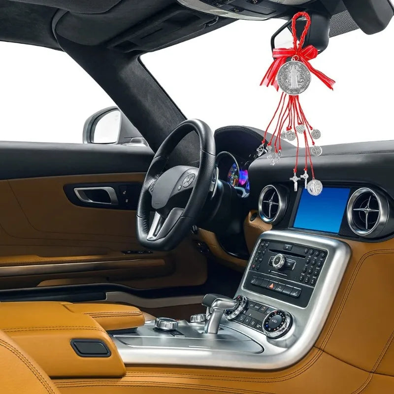 A close-up view of a car interior showing a Saint Benedict Medal Protection Charm hanging from the rearview mirror.