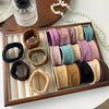 A wooden tray holds various extra-wide elastic hair bands in shades of pink, purple, beige, and green.