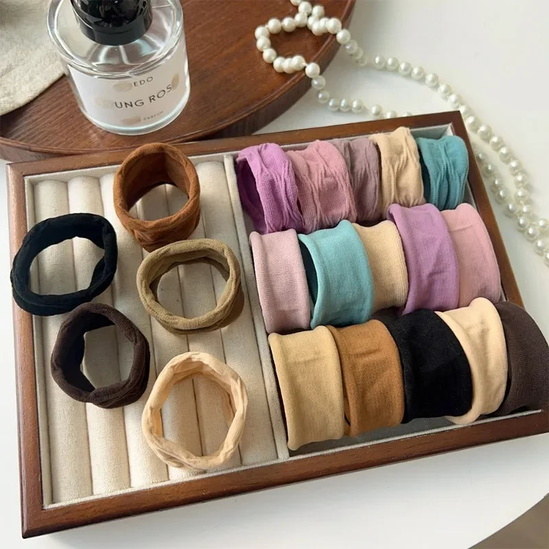 A wooden tray holds various extra-wide elastic hair bands in shades of pink, purple, beige, and green.