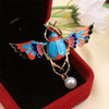 Broche couleur or avec motif d'abeille bleue et orange aux ailes irisées sur fond de velours rouge foncé.