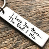 Silver keychain tag engraved with the message I Love You More I Win on a wooden surface.