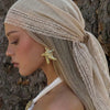 A woman wearing a beige bohemian lace trim shawl draped over her head and hair, featuring a gold starfish earring.