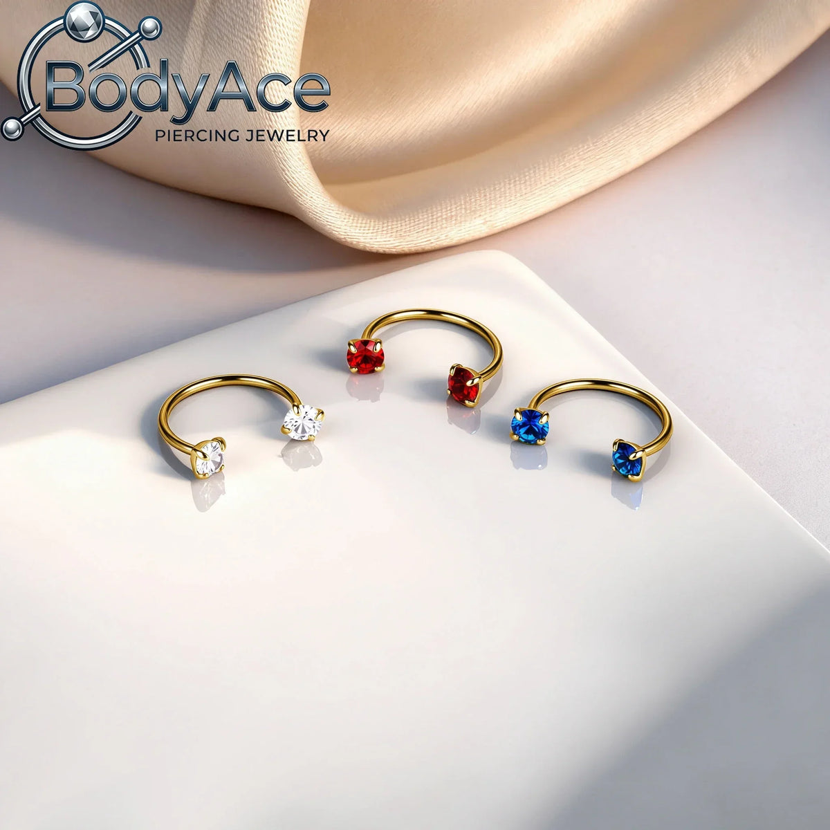 Gold-toned titanium steel nose rings featuring red, blue, and clear cubic zirconia crystals displayed on a white surface.